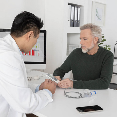 Ihre Inhalationstherapie im Blick Ein Arzt und ein Patient in einer Praxisumgebung betrachten gemeinsam einen eTrack Controller. Ein Smartphone liegt auf einem Schreibtisch